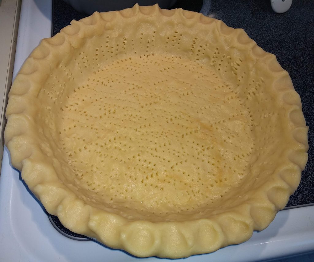 uncooked pie crust in dish, edges shaped and holes punched